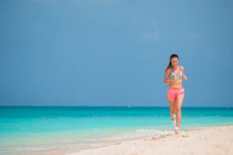 A woman runs on a beach with turquoise water and a clear blue sky