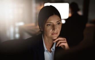 A woman in a suit with a pensive expression, resting her chin on her hand