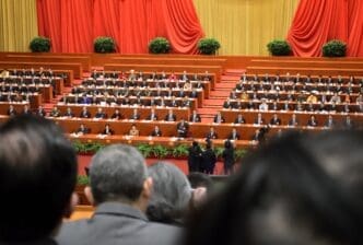 Officials seated in a large hall with red curtains and potted plants