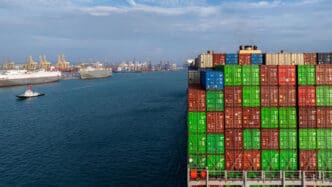 Stacked shipping containers on a cargo ship with a port in the background
