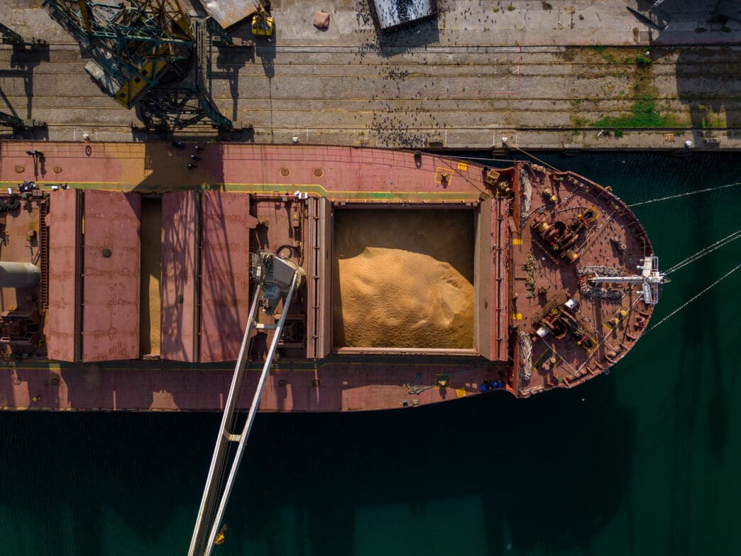 An aerial view of a cargo ship being loaded with grain at a port