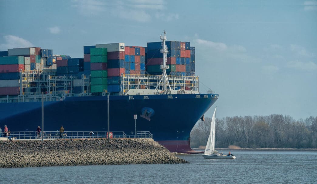 A large cargo ship passes a sailboat on a body of water