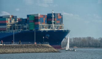 A large cargo ship passes a sailboat on a body of water