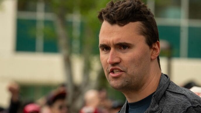A man with short, brown hair wearing a dark jacket speaks with his mouth slightly open