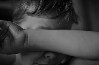 Close-up of a child's face partially obscured by their arm
