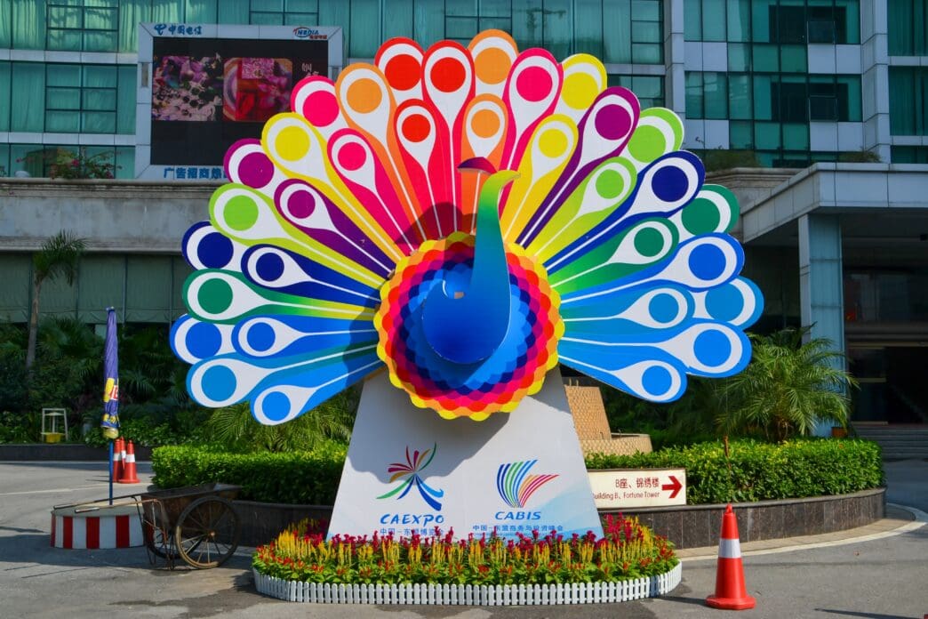 A colorful, artistic sculpture of a peacock with an expansive fan of feathers on display in front of a building in Nanning, China