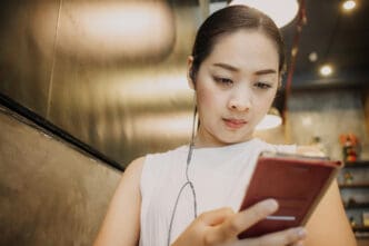 A Chinese woman with earbuds uses her phone in a cafe