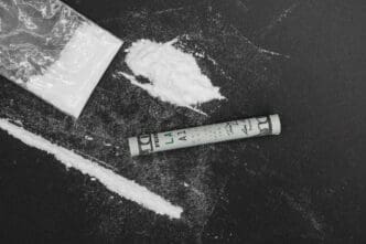 Rolled up dollar bill next to a pile of white powder and a plastic bag