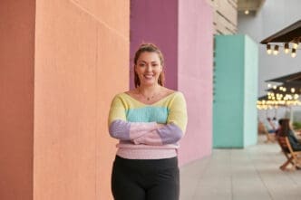 A smiling woman with arms crossed stands in front of colorful walls