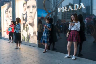 Consumers on a sidewalk in front of a Prada store and large billboards in Chengdu, China