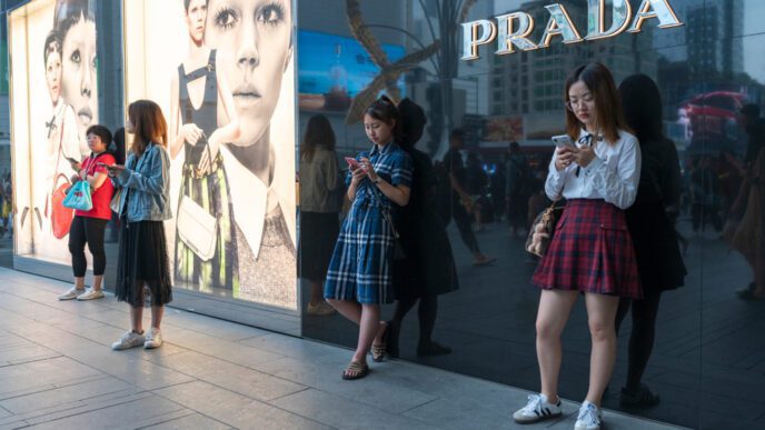 Consumers on a sidewalk in front of a Prada store and large billboards in Chengdu, China