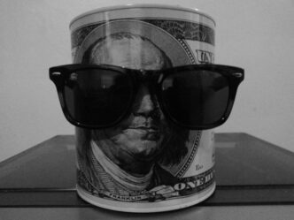 A black and white image of a canister with a Benjamin Franklin portrait wearing sunglasses
