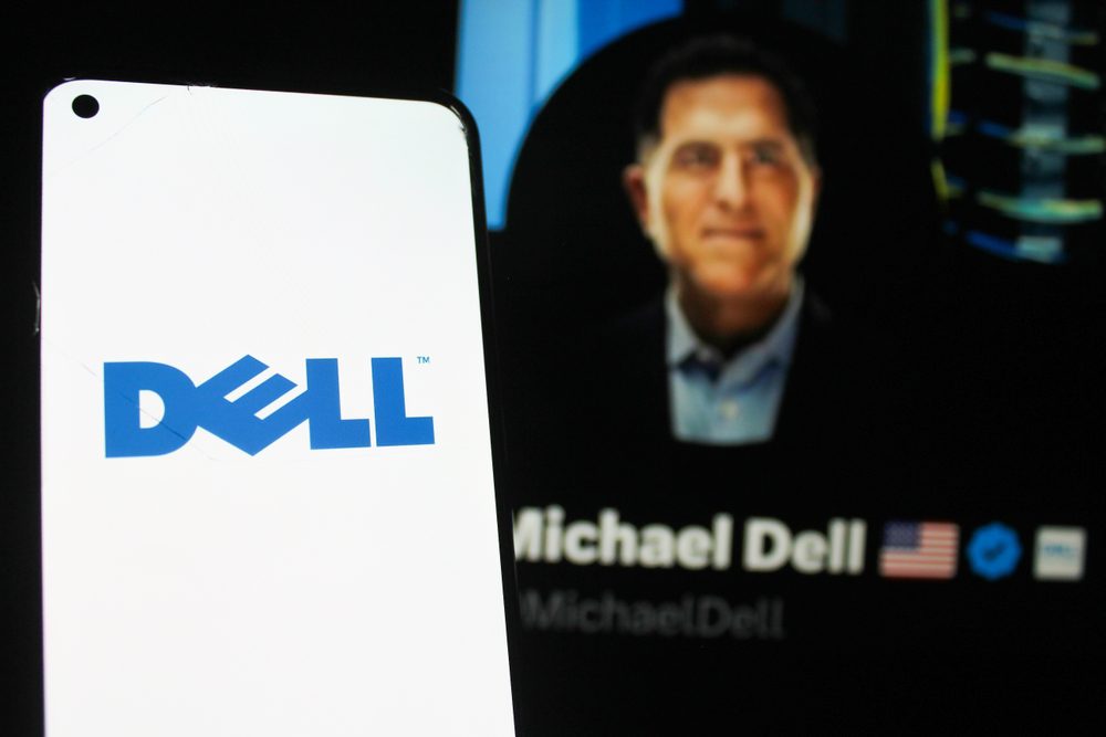 The Dell logo on a smartphone in the foreground with a blurred photo of Michael Dell in the background