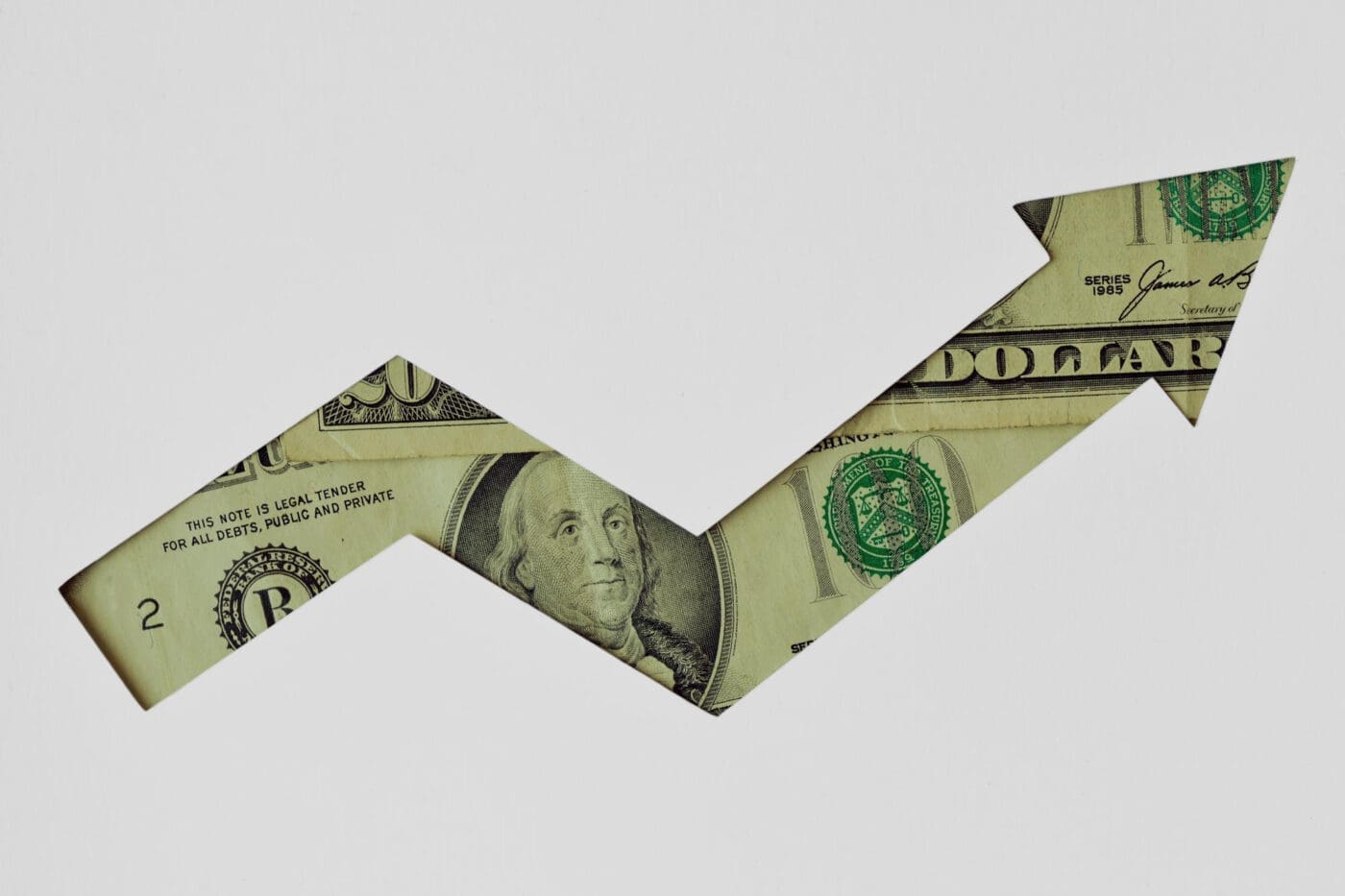 Arrow shape cut out of a dollar bill pointing upwards on a white background