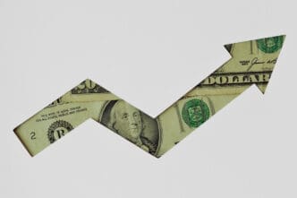 Arrow shape cut out of a dollar bill pointing upwards on a white background