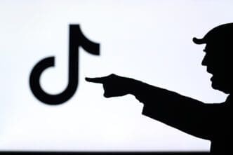 The silhouette of a person pointing a finger at a blurred TikTok logo on a screen