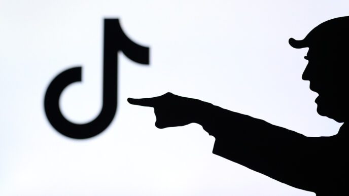 The silhouette of a person pointing a finger at a blurred TikTok logo on a screen