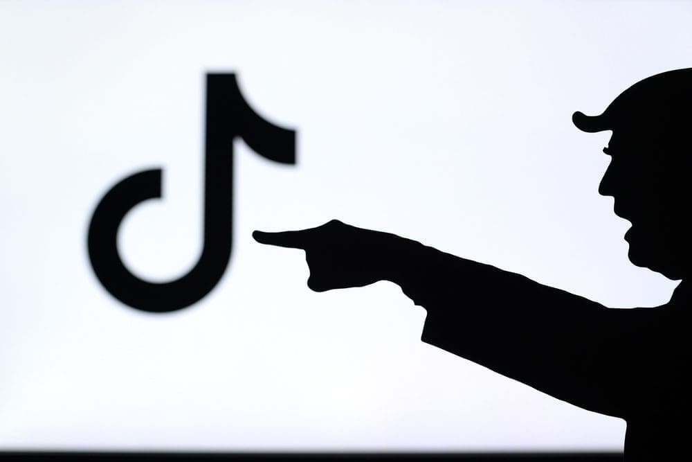 The silhouette of a person pointing a finger at a blurred TikTok logo on a screen