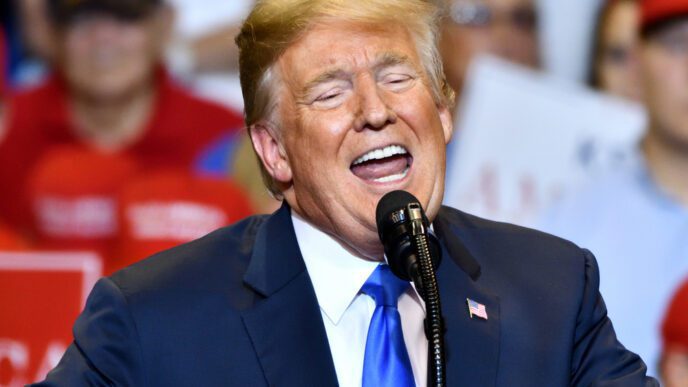Donald Trump speaking at a rally, with his eyes closed and mouth open, in front of a crowd