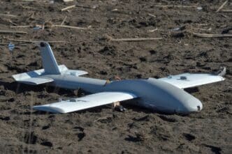 A downed Russian drone, a small, gray aircraft, lies on the muddy ground near a battlefield