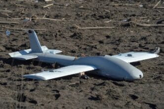 A downed Russian drone, a small, gray aircraft, lies on the muddy ground near a battlefield