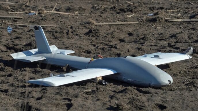 A downed Russian drone, a small, gray aircraft, lies on the muddy ground near a battlefield