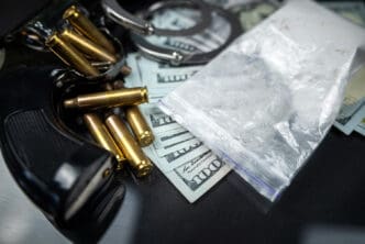 A collection of illegal items including a handgun, bullets, a bag of white powder, and cash on a dark surface