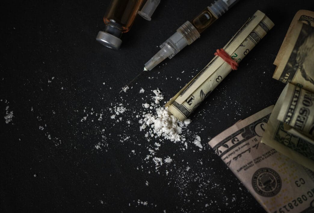Syringe, drugs, and rolled-up dollar bills on a dark surface