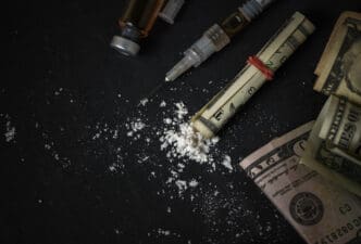 Syringe, drugs, and rolled-up dollar bills on a dark surface
