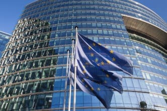 The European Union flag waves in front of a modern glass building