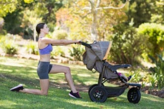 A young woman performs a lunge while using a baby stroller for balance in a sunny park
