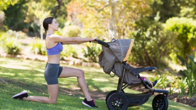 A young woman performs a lunge while using a baby stroller for balance in a sunny park