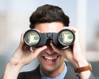 A man in a suit looks through binoculars reflecting $100 bills