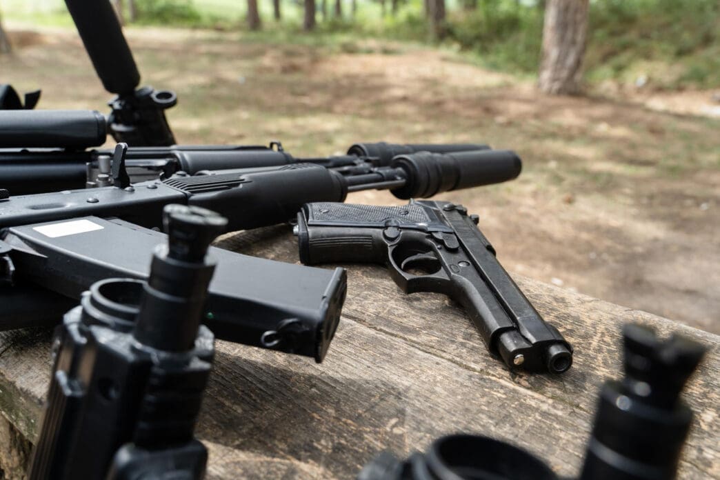 A collection of firearms and accessories on a wooden surface in a forest setting