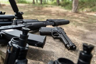 A collection of firearms and accessories on a wooden surface in a forest setting