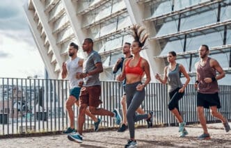 A diverse group of six friends jogging together on a concrete path next to a modern building