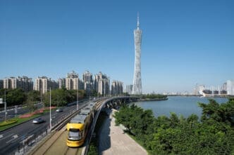A yellow tram passes by a tower and cityscape in Guangzhou under a clear blue sky.