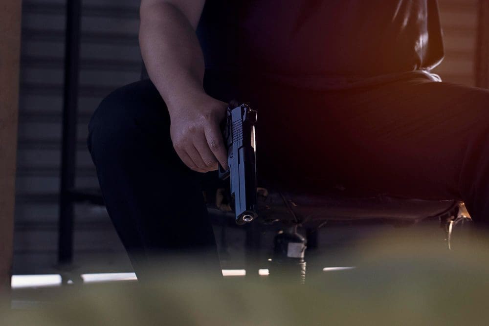 A person is sitting down and holding a handgun, with a focus on the weapon