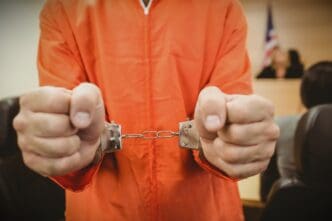 A person in an orange jumpsuit is handcuffed in a courtroom
