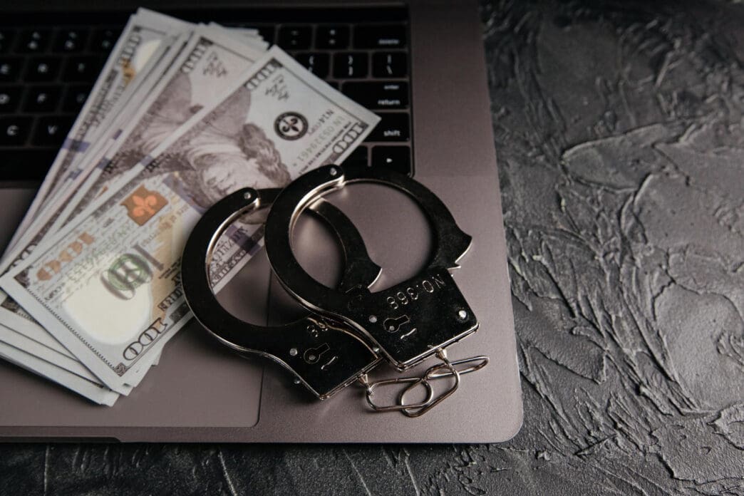 Handcuffs and money lie on a laptop keyboard