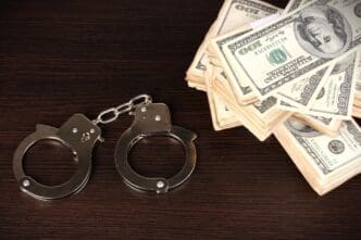 A pair of handcuffs lying next to a large stack of US hundred-dollar bills on a dark wooden surface.