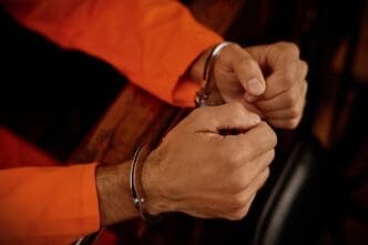 A close-up of a person's hands in handcuffs, wearing an orange jumpsuit