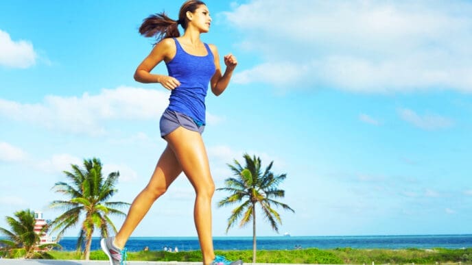 A woman with a determined expression jogs on a sunny day with palm trees in the background