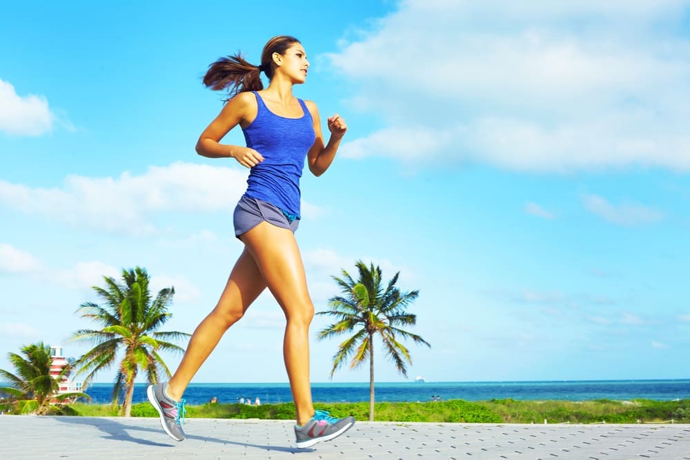 A woman with a determined expression jogs on a sunny day with palm trees in the background