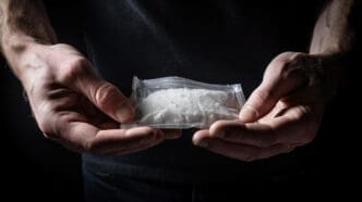 A person holds a transparent plastic bag containing a white, crystalline substance.