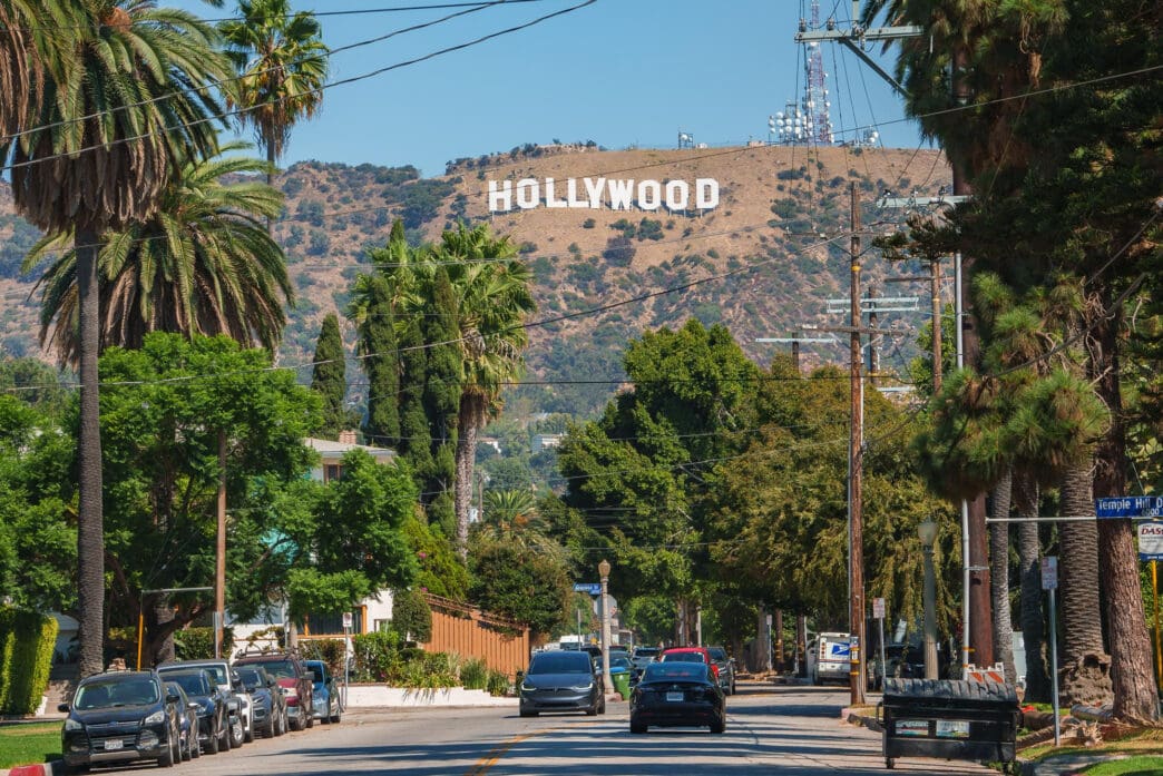 The Hollywood sign is visible on a hill above a street with palm trees