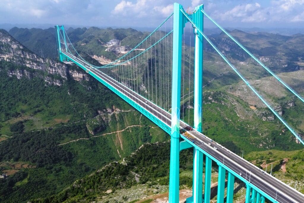 The massive Huajiang Canyon Bridge spans a deep, green canyon under a cloudy sky