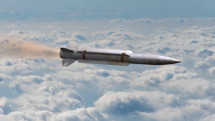 A missile flies through clouds, leaving a trail of smoke
