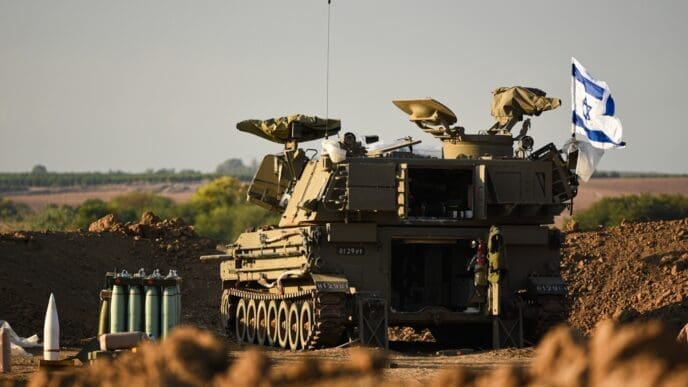 An IDF M109 artillery cannon is positioned on a dirt mound with an Israeli flag, prepared to fire