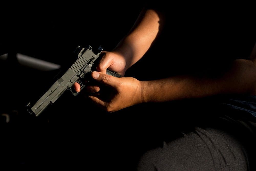 A person is sitting in a dark room holding a handgun, with a focus on their hand
